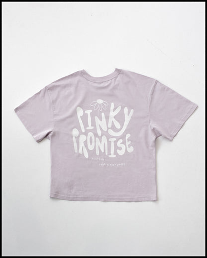 Fliederfarbenes T-Shirt mit großem weißen Rückendruck. Über dem Schriftzug „PINKY PROMISE“ ist eine stilisierte Blume platziert. Darunter steht in kleiner Schrift „CLOTHING FROM PLANET EARTH“.