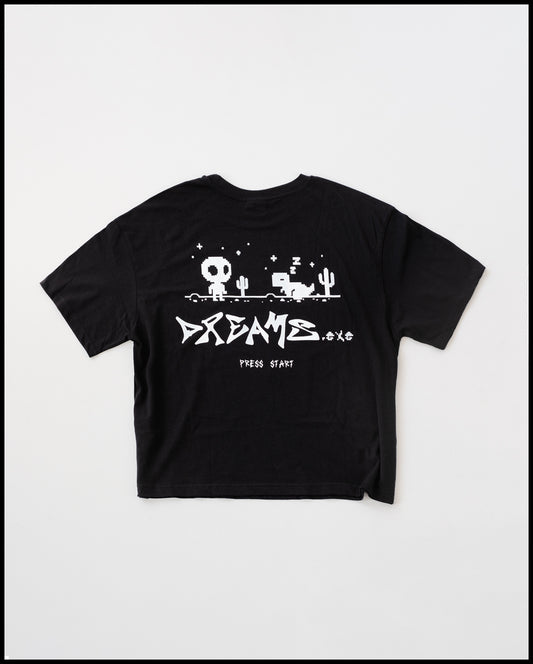 Schwarzes T-Shirt mit großem weißen Rückendruck im Pixel-Art-Stil. Das Motiv zeigt eine Spiellandschaft mit Kaktus, einem stehenden Figur-Charakter mit großem Kopf sowie einem schlafenden Pixel-Tier. Darunter steht in markanter Schrift „DREAMS.exe“ und klein „PRESS START“.