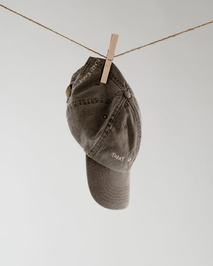 Braune Baseballcap hängt an einer Leine, mit weißem Schriftzug „Today is a good day“ auf der Front und „Planet Earth“ an der Seite.