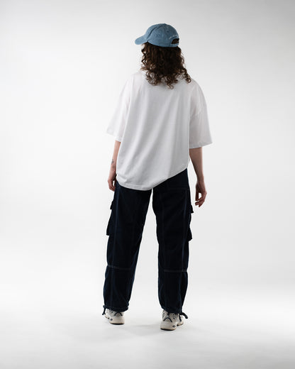 Rückansicht der gleichen Person mit weißem T-Shirt ohne Rückendruck, blauer Cap und dunkler Hose mit weißer Kontrastnaht.