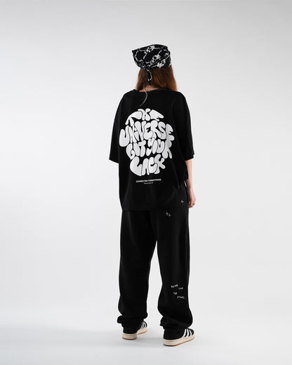 Frau mit schwarzem Bandana trägt ein schwarzes T-Shirt mit großem weißen Schriftzug auf dem Rücken: „The Universe Got Your Back“