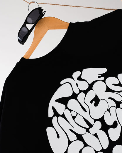 Schwarzes T-Shirt mit weißem Rückseitendruck „The Universe Got Your Back“, hängend an einem Holzkleiderbügel mit Sonnenbrille