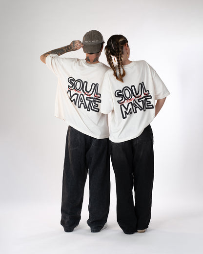 Zwei Personen stehen nebeneinander und tragen weiße Oversized-T-Shirts mit schwarzem und rotem Rückendruck „Looking for my Soul Mate“. Beide kombinieren die Shirts mit weiten schwarzen Jeans – moderner Unisex-Partnerlook im entspannten Streetwear-Stil.