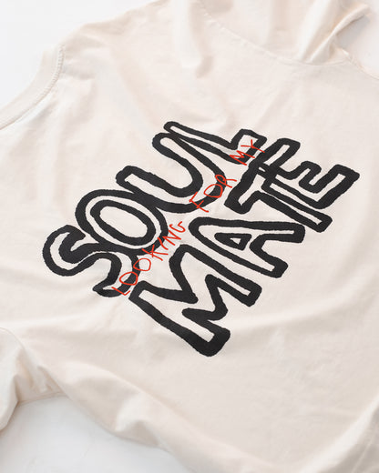 Detailaufnahme eines weißen T-Shirts mit großem schwarzen und roten Rückendruck „Looking for my Soul Mate“. Das Shirt liegt flach auf hellem Hintergrund – modernes Unisex-Design mit auffälliger Typografie im Streetwear-Stil.