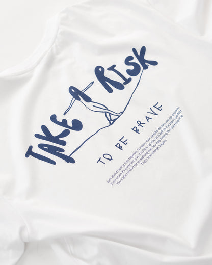 Weißes T-Shirt mit blauem Rückendruck „Take a Risk – To Be Brave“. Das Design zeigt eine stilisierte Figur auf einem Seil und darunter einen motivierenden Text – minimalistisches, inspirierendes Streetwear-Design, flach auf hellem Hintergrund präsentiert.
