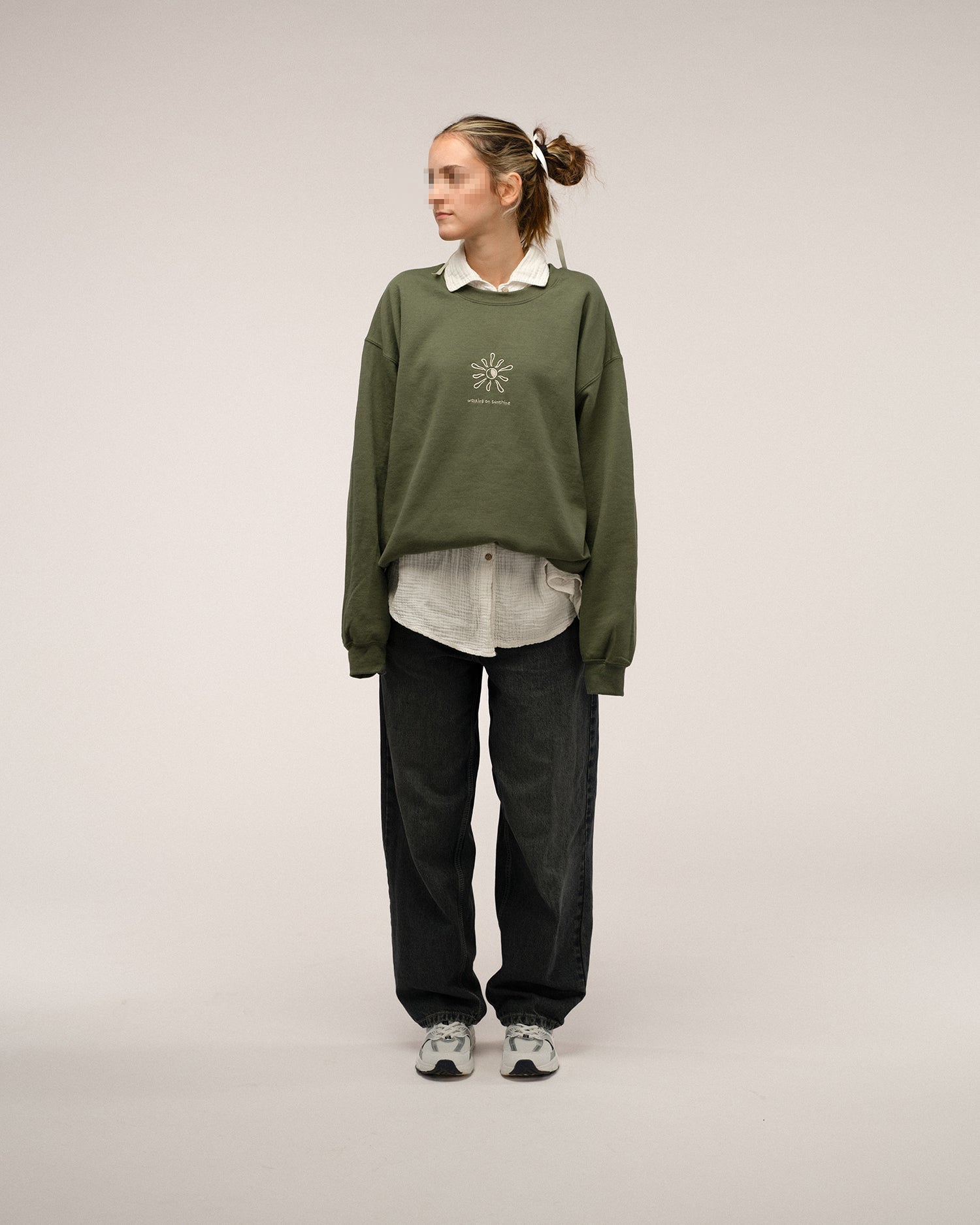  Grünes Sweatshirt mit beiger Stickerei „walking on sunshine“ und Sonnenmotiv auf der Brust, kombiniert mit dunkler Jeans und heller Bluse.
