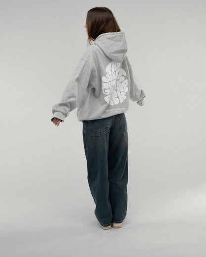 Person von hinten in einem grauen Kapuzenpullover mit großem weißem Rückendruck. Der Print zeigt die Worte „THE UNIVERSE GOT YOUR BACK“ in verspielter Typografie. Der untere Teil des Schriftzugs ist leicht von der Körperhaltung verdeckt.