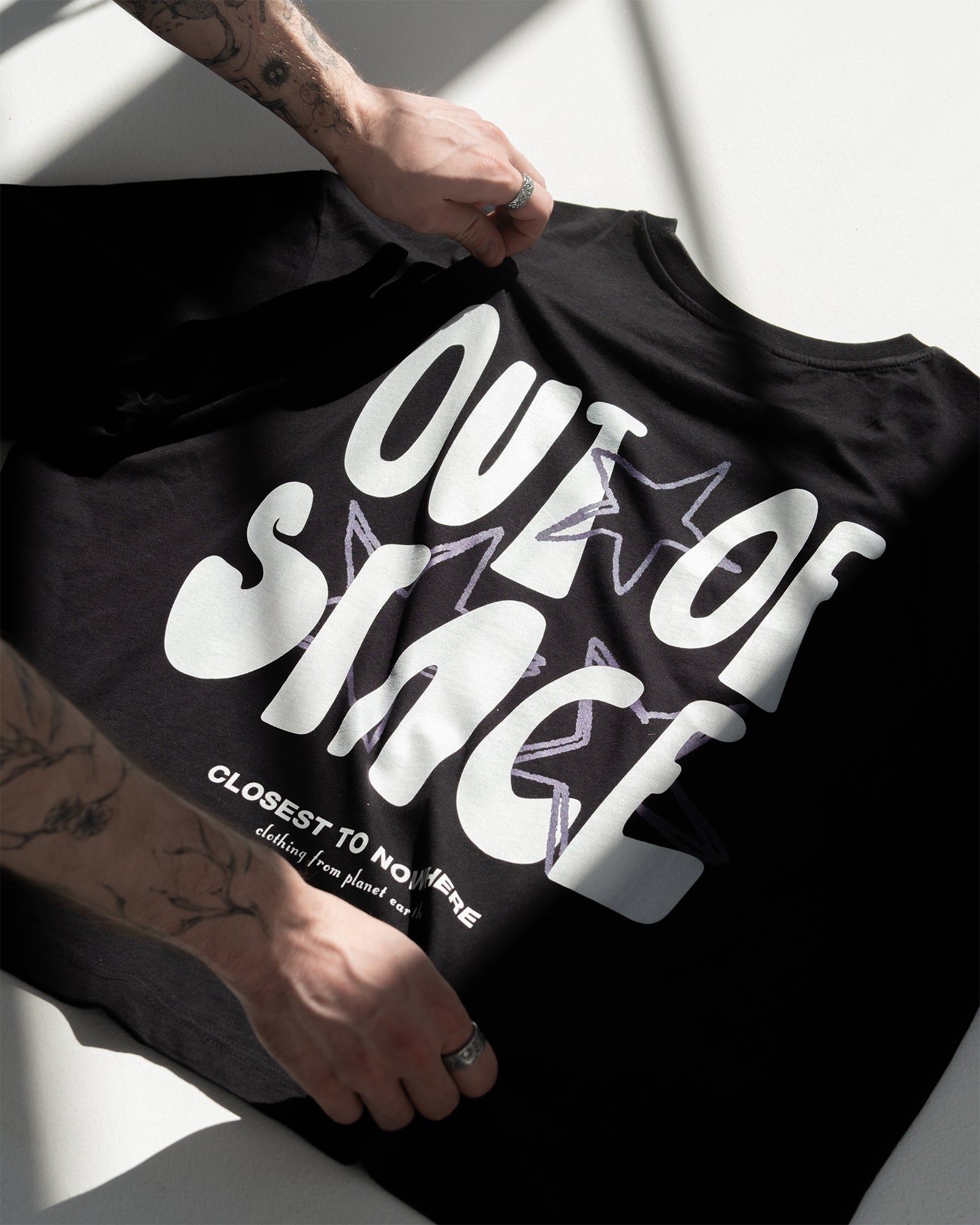 Detail Rückenprint im Flatlay: weißer Großschriftzug „OUT OF SPACE“ mit lila Stern-Outline; darunter „CLOSEST TO NOWHERE – clothing from planet earth“.