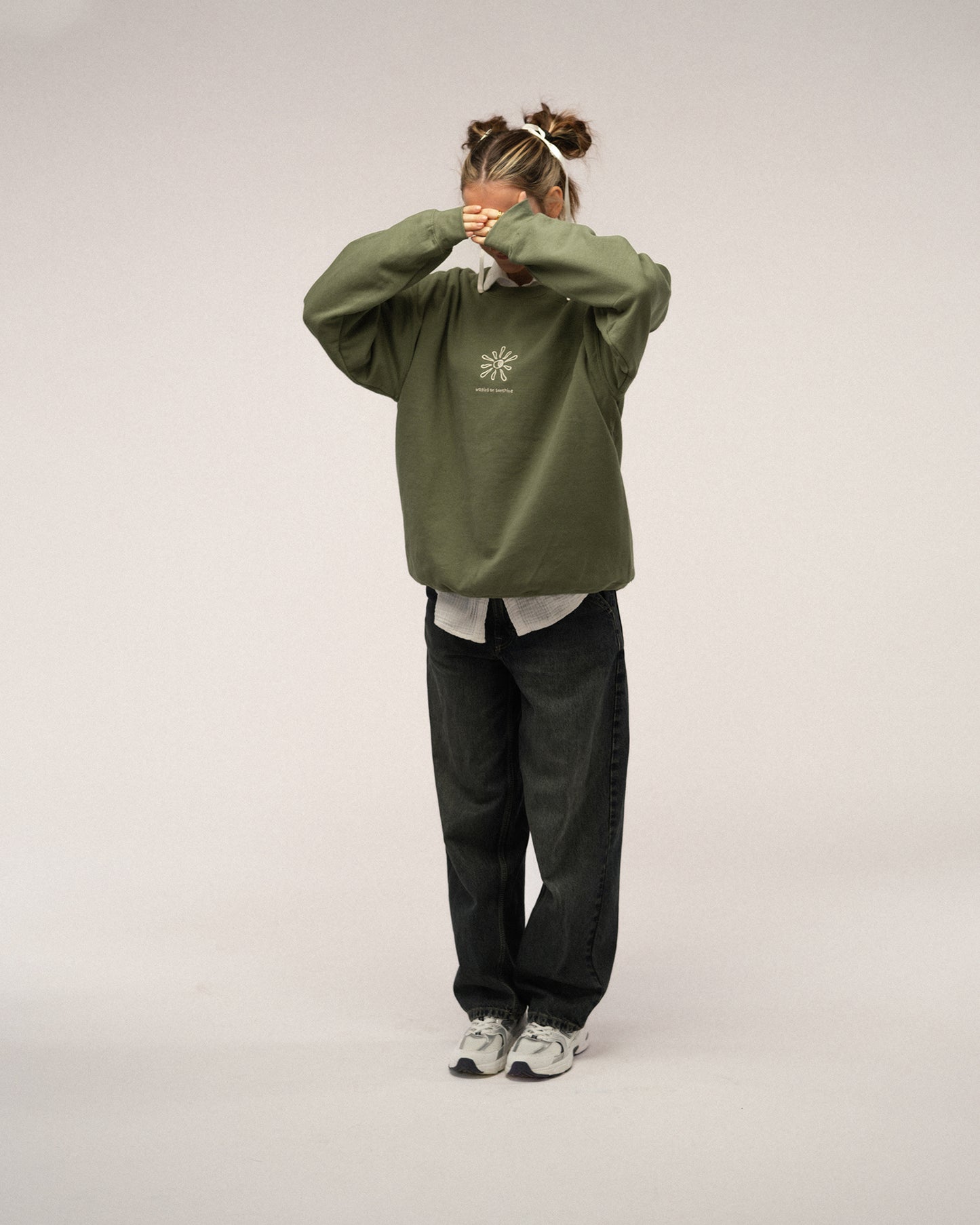 Grünes Sweatshirt mit beiger Stickerei „walking on sunshine“ und Sonnenmotiv auf der Brust, kombiniert mit dunkler Jeans und heller Bluse.