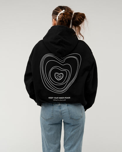Schwarzer Hoodie mit Rückenmotiv aus weißen Linien in Herzform und dem Schriftzug „KEEP YOUR INNER PEACE – clothing from planet earth“, getragen von einer Frau mit heller Schleife im Haar.