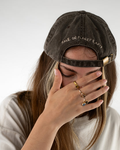 Rückansicht einer getragenen braunen Cap mit dem gestickten Schriftzug „Made on planet Earth“ über dem verstellbaren Metallverschluss.