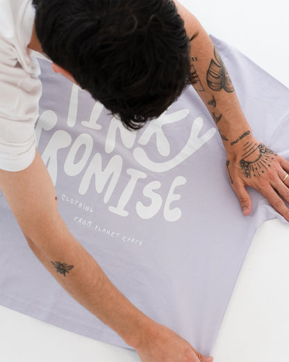 Nahaufnahme des Rückenprints auf fliederfarbenem T-Shirt: großer weißer Schriftzug „PINKY PROMISE“, darunter „clothing from planet earth“.