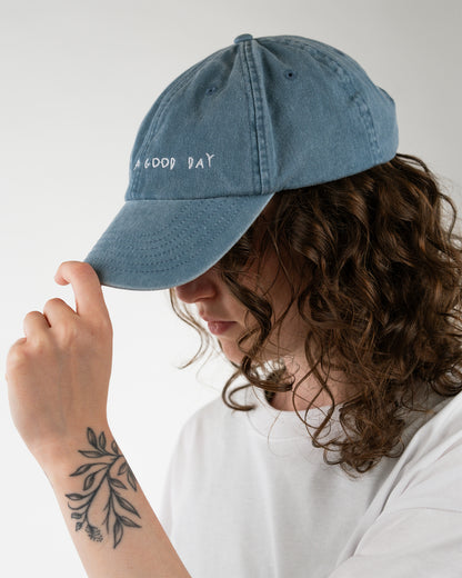 Vorderansicht einer getragenen, blauen Cap mit weißer Stickerei „Today is a good day“ auf der Front.