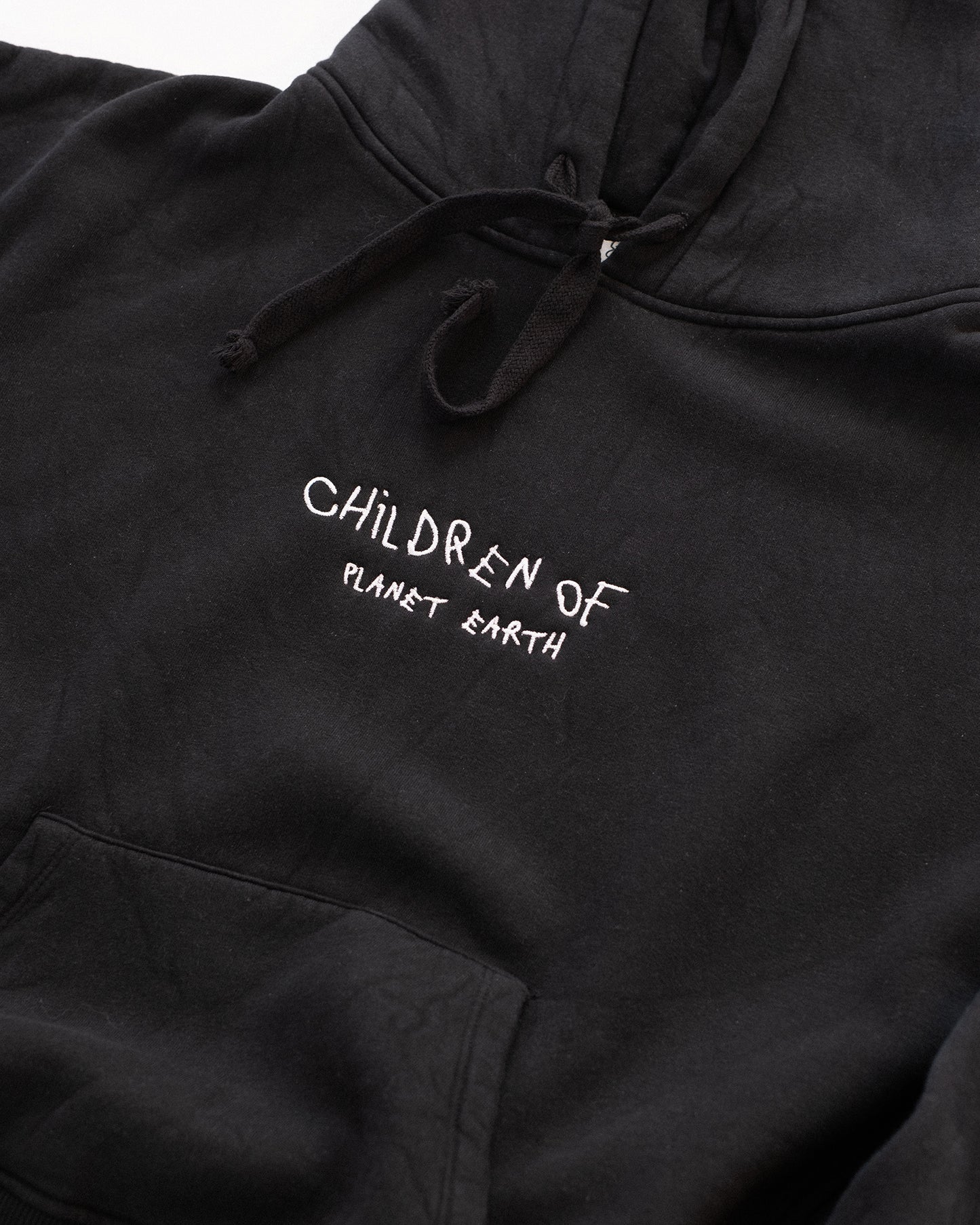 Schwarzer Hoodie mit weißer Stickerei auf der Brust: „Children of Planet Earth“. Nahaufnahme der Vorderseite mit Kapuze und Kängurutasche, flach auf weißem Hintergrund platziert – minimalistisches Design mit nachhaltigem Streetwear-Look.