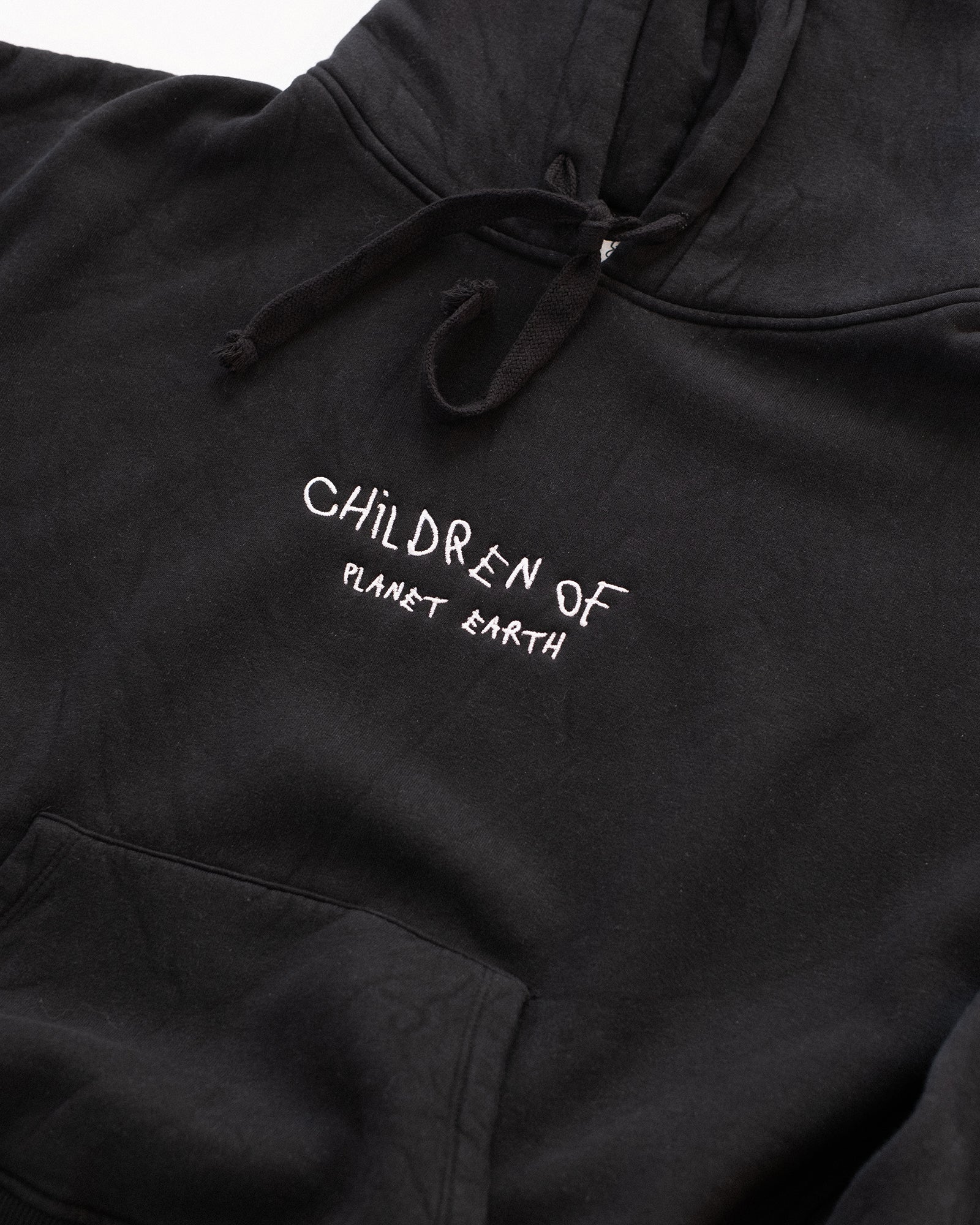 Schwarzer Hoodie mit weißer Stickerei auf der Brust: „Children of Planet Earth“. Nahaufnahme der Vorderseite mit Kapuze und Kängurutasche, flach auf weißem Hintergrund platziert – minimalistisches Design mit nachhaltigem Streetwear-Look.