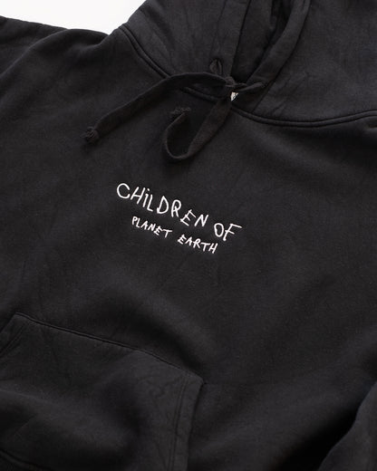 Schwarzer Hoodie mit weißer Stickerei auf der Brust: „Children of Planet Earth“. Nahaufnahme der Vorderseite mit Kapuze und Kängurutasche, flach auf weißem Hintergrund platziert – minimalistisches Design mit nachhaltigem Streetwear-Look.