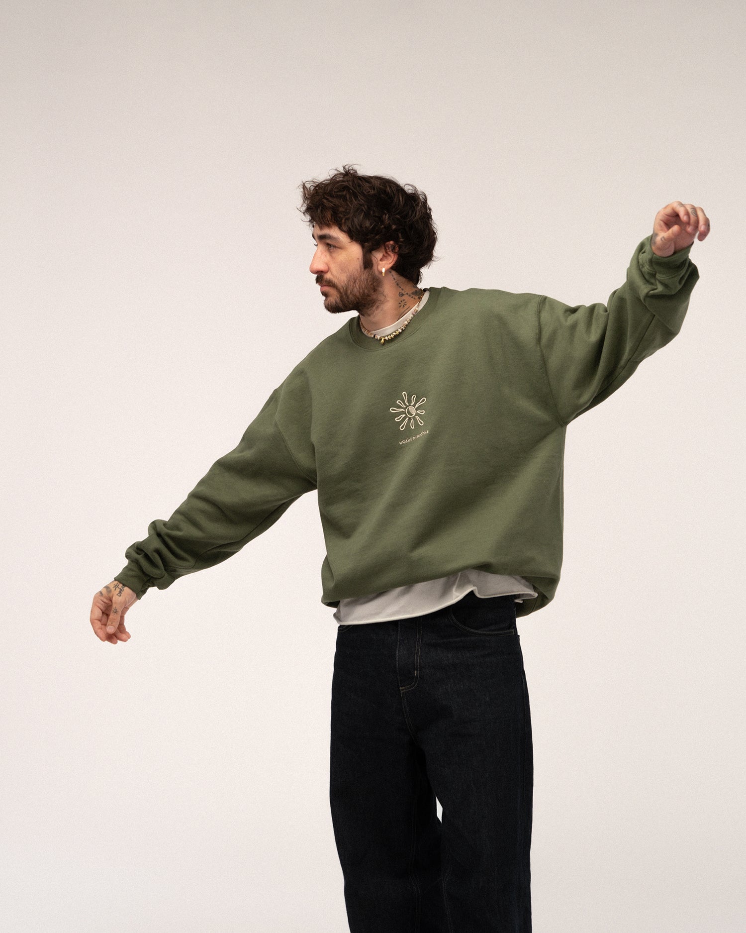 Grünes Sweatshirt mit aufgestickter Sonne und Text „walking on sunshine“, getragen von einer Person in Bewegung mit weit ausgestreckten Armen.