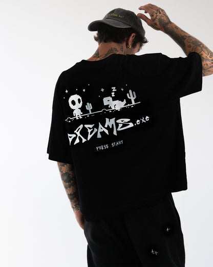 Rückenansicht des schwarzen Oversize-T-Shirts: großflächiger weißer Pixel-Print (Figur, Kaktus, schlafendes Tier, Sterne) mit markantem „DREAMS“-Schriftzug und „PRESS START“; weicher, weiter Fall des Stoffes.