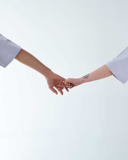 Minimalistische Szene: zwei ausgestreckte Arme, kleine Finger ineinander gehakt – Symbol „Pinky Promise“ vor hellem Hintergrund.