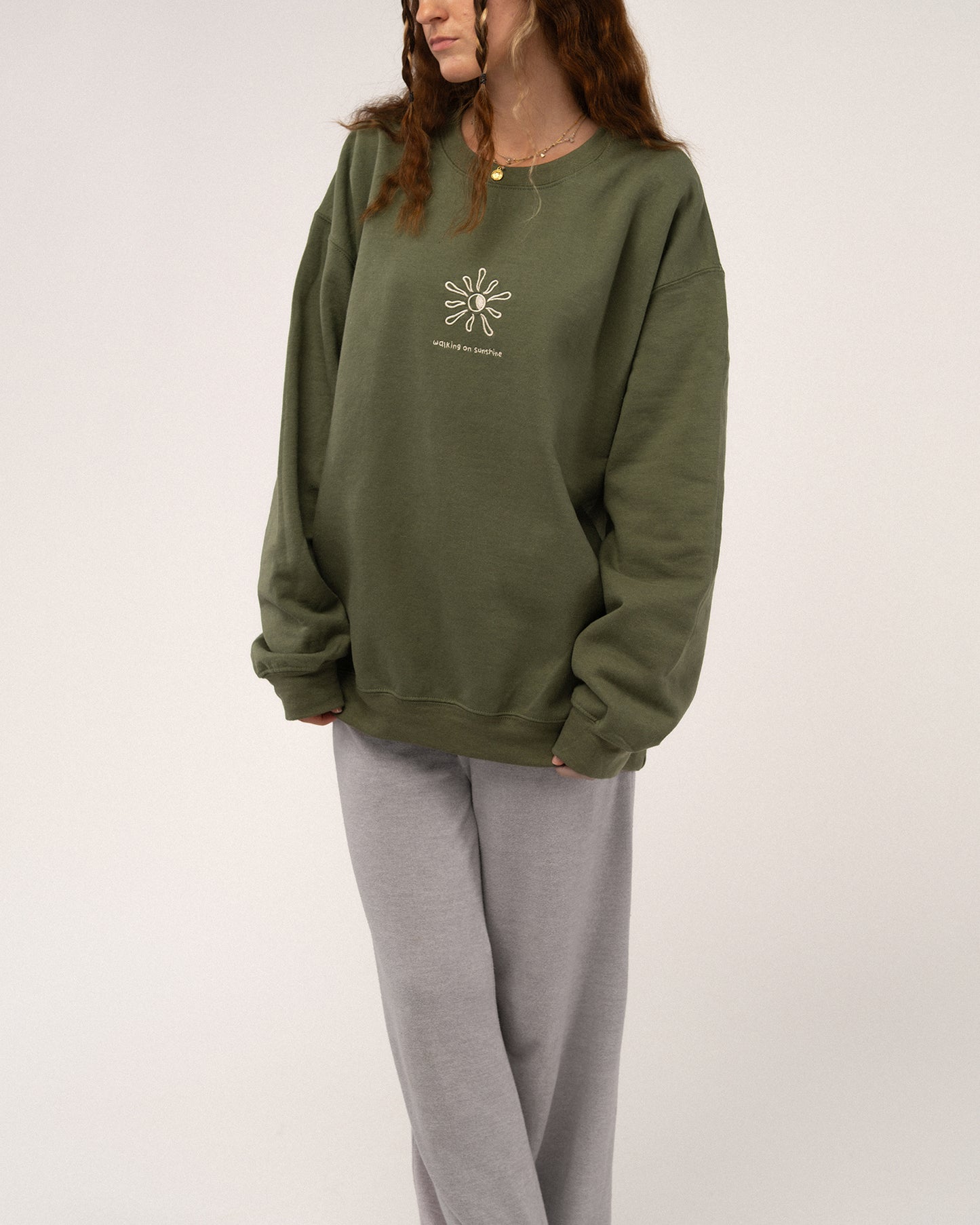 Grünes Sweatshirt mit beiger Stickerei „walking on sunshine“, kombiniert mit grauer Jogginghose für einen lässigen Look.