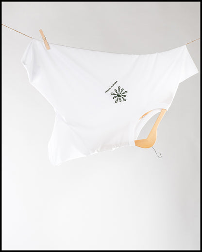 Weißes T-Shirt, aufgehängt auf einem Holzkleiderbügel und einer Wäscheleine, seitlich fixiert mit einer Holzklammer. In der Mitte des T-Shirts befinmdet sich eine Sonnenform mit dem Text ‚WALKING ON SUNSHINE‘.