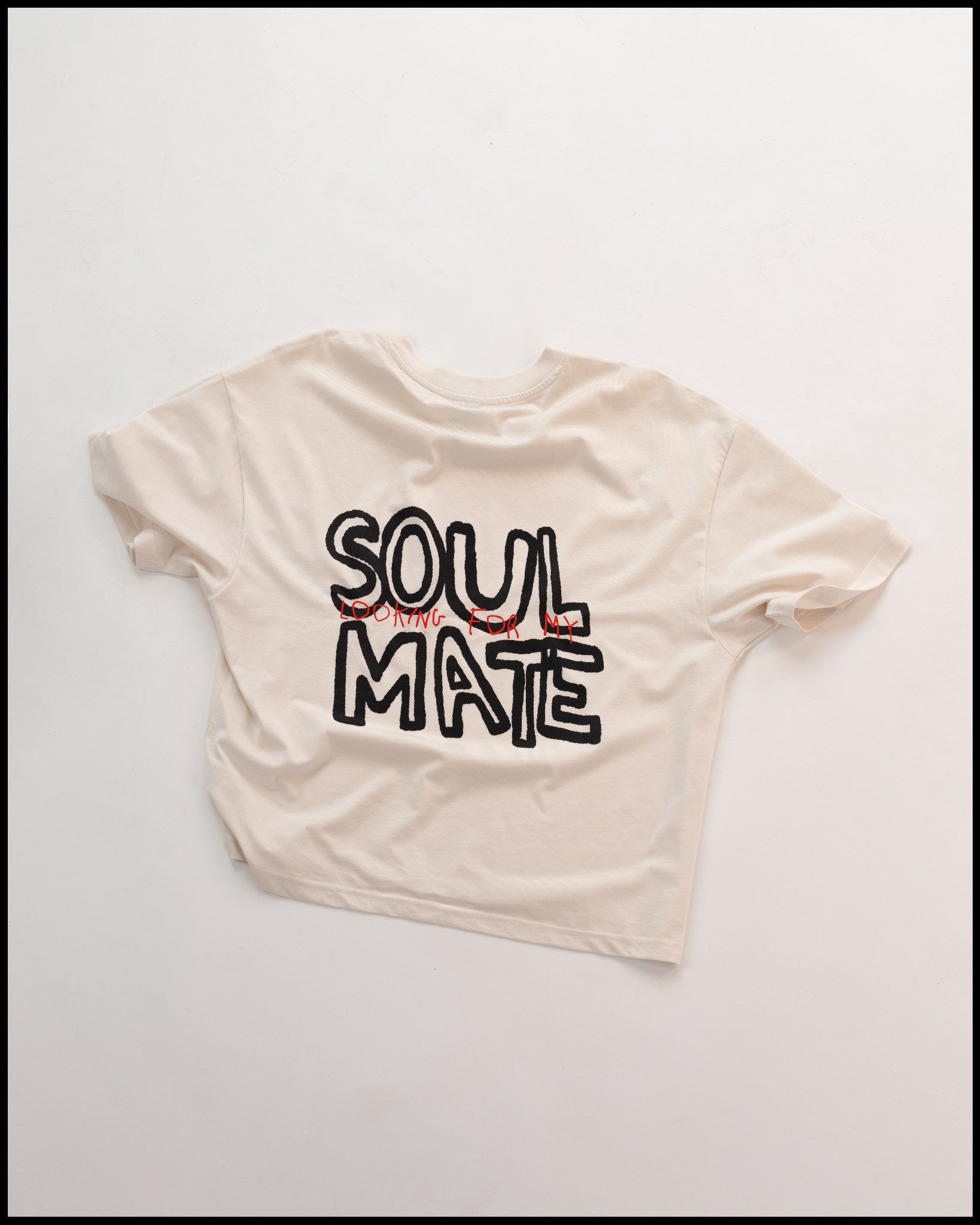 Weißes T-Shirt mit großem schwarzen Schriftzug „SOUL MATE“ auf der Rückseite und rotem Zusatztext „LOOKING FOR MY“ in handgeschriebener Optik. Locker geschnitten, modernes Streetwear-Design mit künstlerischem Schriftstil.