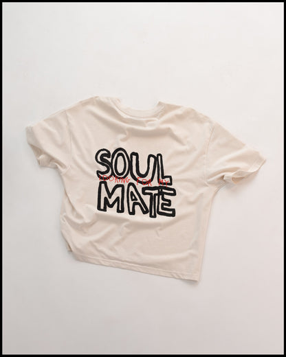 Weißes T-Shirt mit großem schwarzen Schriftzug „SOUL MATE“ auf der Rückseite und rotem Zusatztext „LOOKING FOR MY“ in handgeschriebener Optik. Locker geschnitten, modernes Streetwear-Design mit künstlerischem Schriftstil.