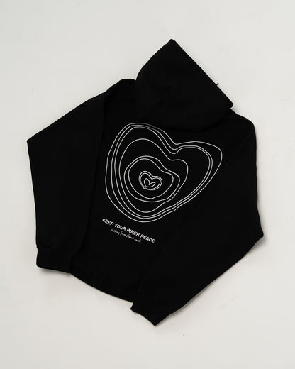 Schwarzer Kapuzenpullover flach auf weißem Hintergrund liegend, Rückseite sichtbar mit weißem Linienherz-Design und dem Aufdruck „KEEP YOUR INNER PEACE – clothing from planet earth“.
